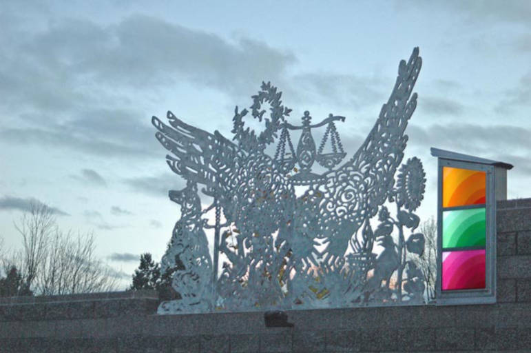 Sculpture featuring many images such as large wings, a K-9 dog and scales and a stainless steel lantern featuring three colorful rectangles of glass