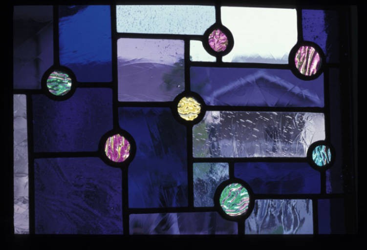 A detail featuring spots of colored dichroic glass on a purple field