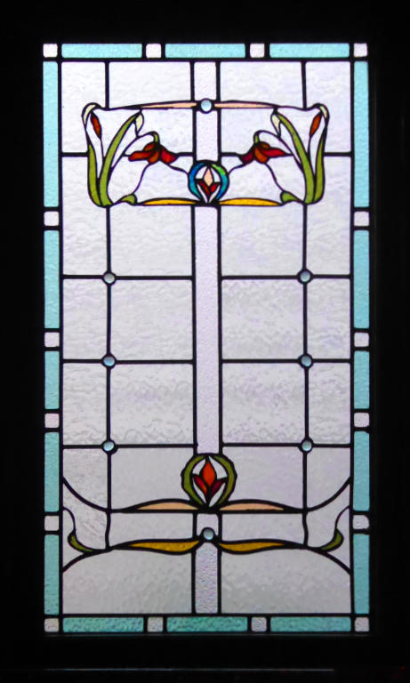 Stained glass with a clear textured background, a blue-green border and upper and lower designs of leaves and flowers